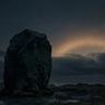A large weathered standing stone sits alone on a barren landscape beneath a dark,