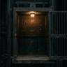 Vintage industrial freight elevator with open steel gate and warm overhead lighting in a dark factory setting.