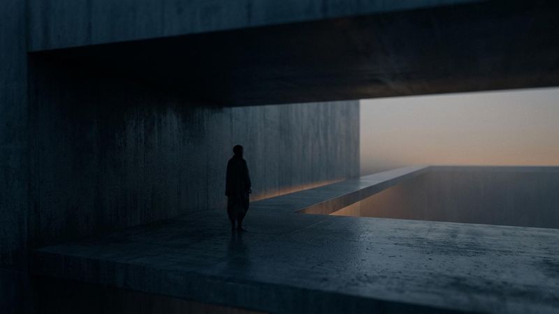 A cinematic, fine-art photograph of a lone, shadowed figure in a brutalist concrete structure at twilight. A narrow bridge of light crosses a vast void toward a distant, hazy horizon. Dark charcoals and blues dominate, accented by a soft, warm amber glow. Film grain and soft-focus effects create a melancholic, transitional mood.
