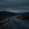A winding road leading through a dark landscape toward a small illuminated building in the distance, symbolizing a long journey toward a goal.