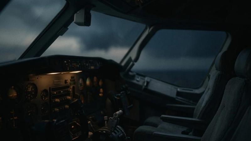Dimly lit airplane cockpit at dusk, showing instruments and empty seats. Dark clouds visible through windows, creating a moody atmosphere.