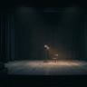 Dark theater stage with a single spotlight illuminating an empty chair, creating a dramatic and minimalist atmosphere